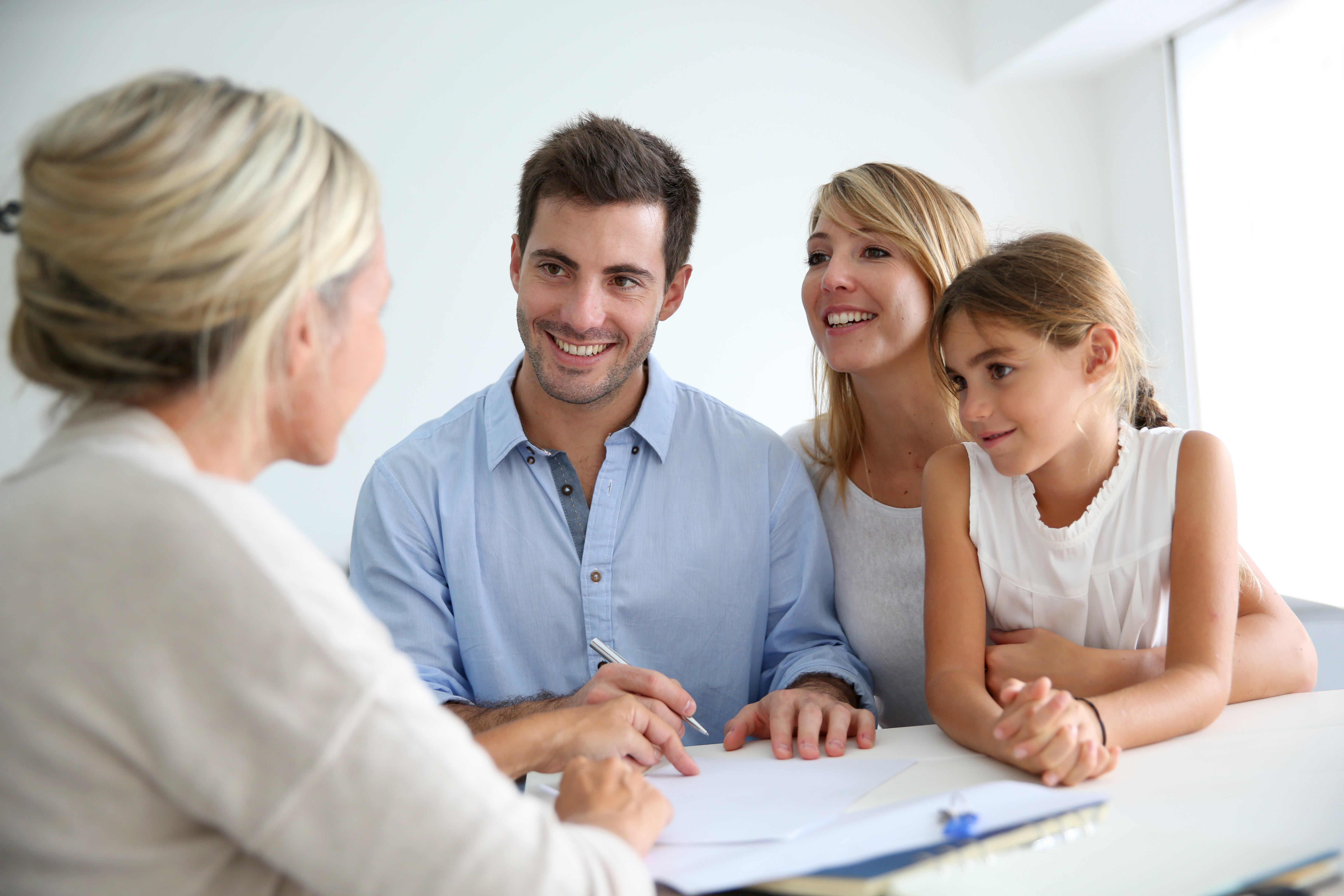 Eine Beraterin sitzt gegenüber einer Familie bestehend aus Mutter, Vater und Kind, welche alle glücklich aussehen.