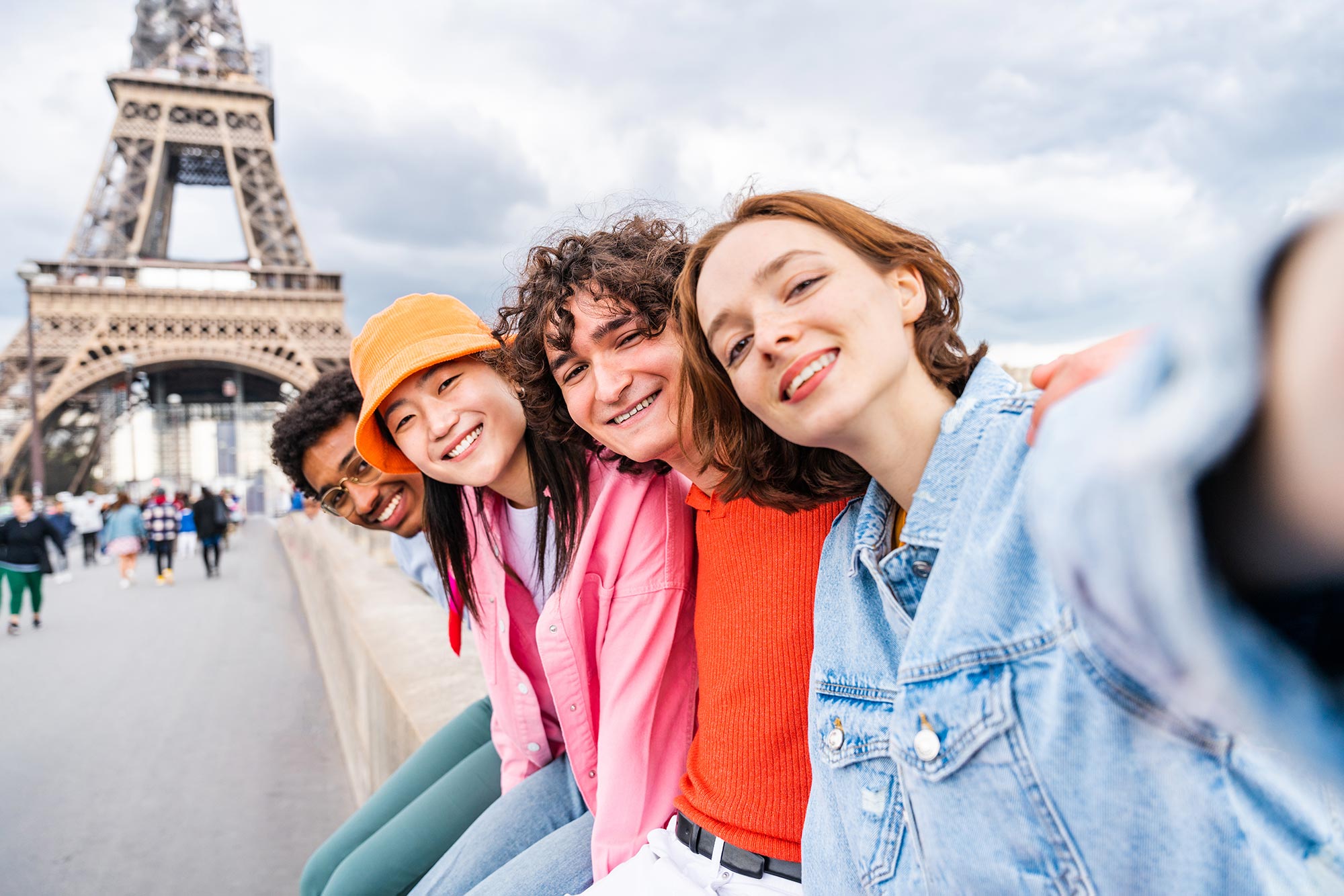 Vier junge Personen lächeln für ein Selfie in die Kamera. Im Hintergrund ist der Eiffelturm zu erkennen.