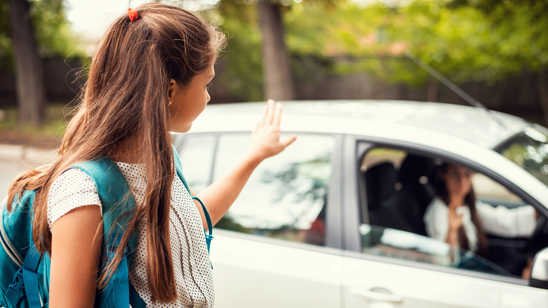Mädchen mit Rucksack verabschiedet sich von ihrer im Auto sitzenden Mutter