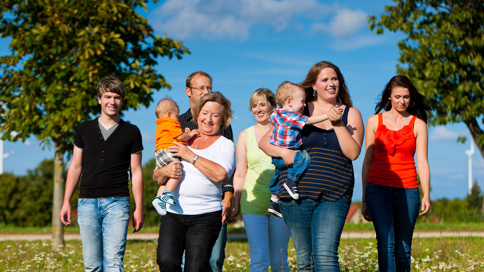 Sechs Menschen im Park, zwei tragen Kinder auf dem Arm, blauer Himmel
