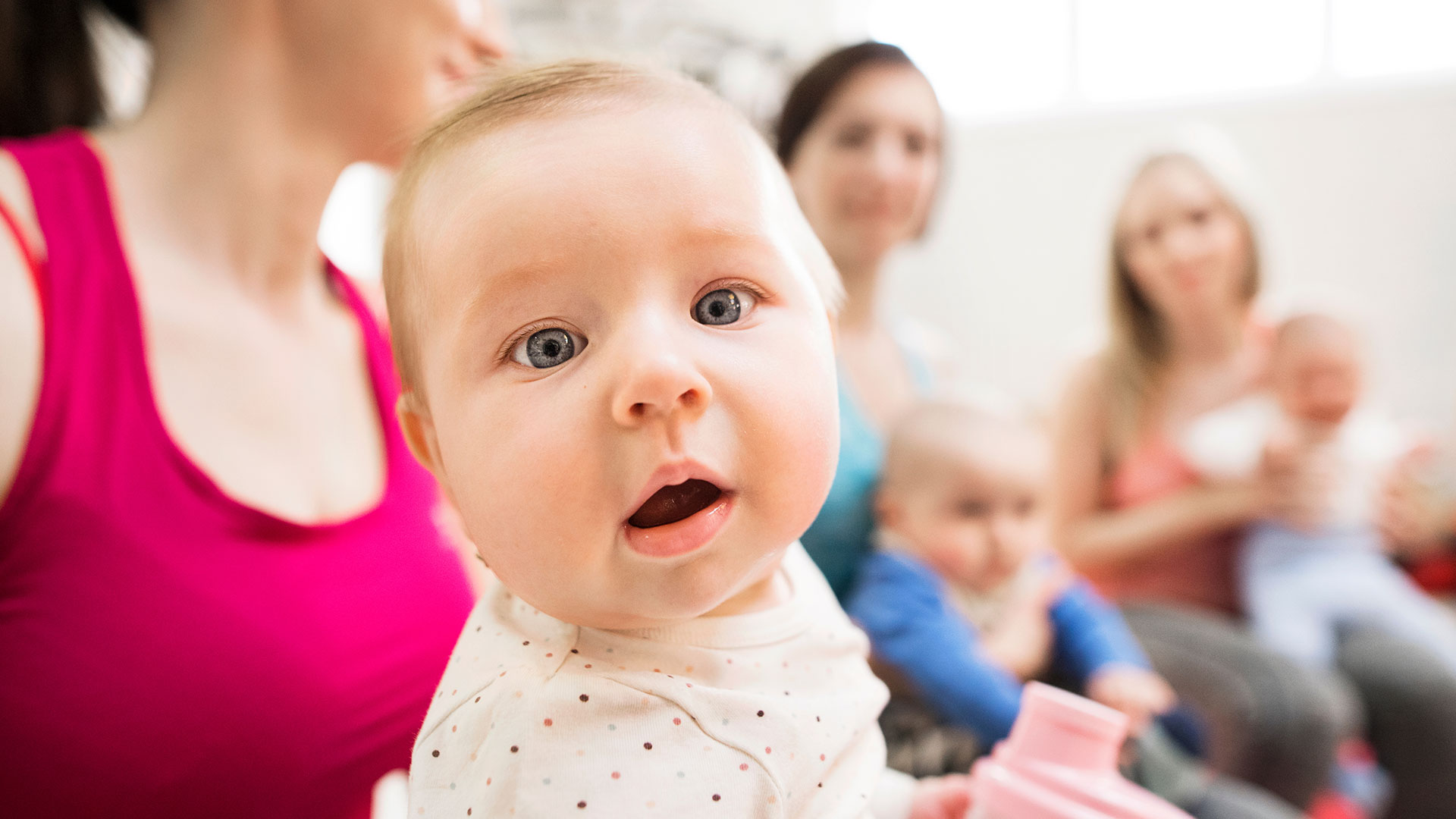 Eine Gruppe Mütter mit ihren Babys bei einem Gruppenangebot. Ein Baby schaut zentral in die Kamera.