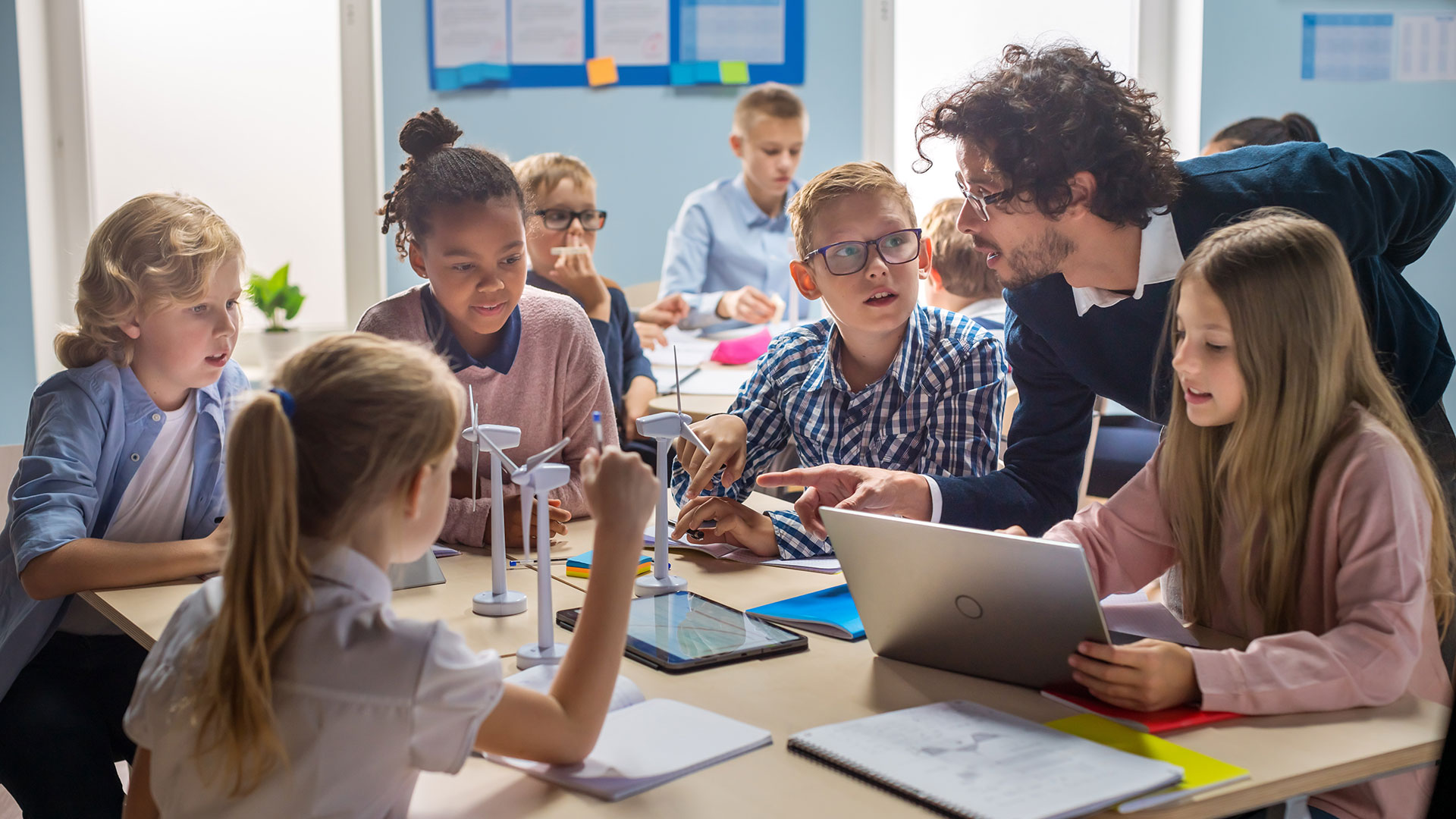 In einer Grundschule lernen Kinder gemeinsam mit ihrem Lehrer an Tablets und Modellen von Windrädern.