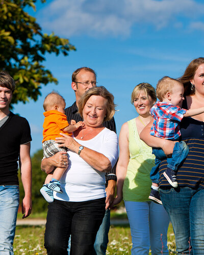 Sechs Menschen im Park, zwei tragen Kinder auf dem Arm, blauer Himmel