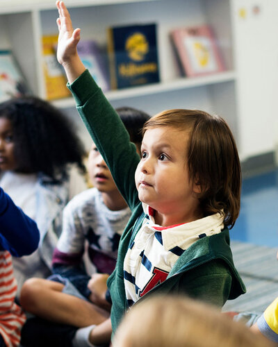 Kinder sitzen auf dem Boden, ein Kind in der Mitte zeigt auf