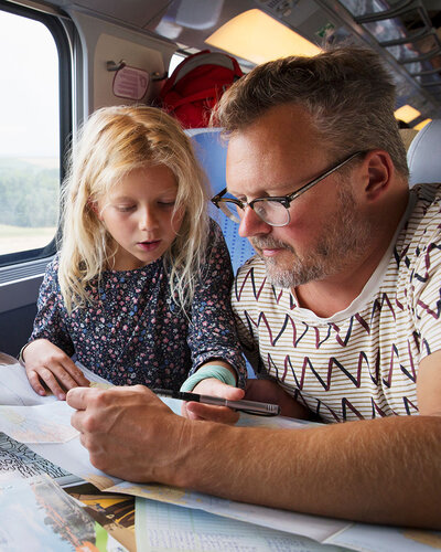 Mann mit Bart und ein Mädchen mit blonden Haaren sitzen an einem Tisch im Zug