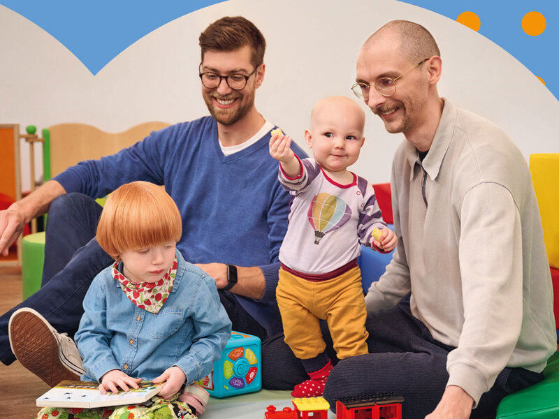 Zwei Väter spielen mit ihren kleinen Kindern auf dem Boden.